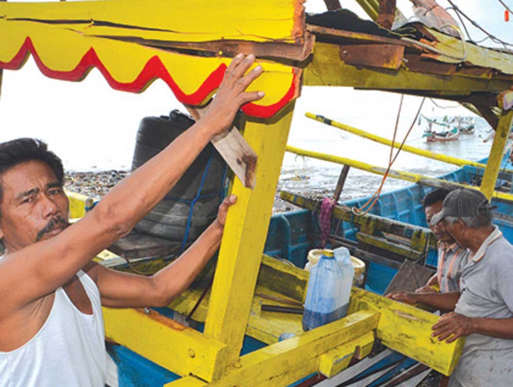 Seorang-nelayan-menunjukkan-bagian-kapal-yang-hancur-setelah-diterjang-ombak-tinggi-di-tepi-Pantai-Satelit,-Dusun-Palurejo,-Desa-Tembokrejo,-Kecamatan-Muncar,-kemarin