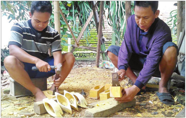 Saji-dan-Sugeng-memahat-lonceng-sapi-yang-terbuat-dari-kayu-nangka-di-Dusun-Cempokosari,-Desa-Sarimulyo