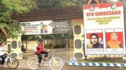 Poster-sosialisasi-Pilkades-Kepundungan-yang-dipasang-di-depan-kantor-desa-berisi-gambar-dua-kandidat-Kepala-Desa-Kepundungan,-Tri-Marvila-Sukmana-dan-Murti.